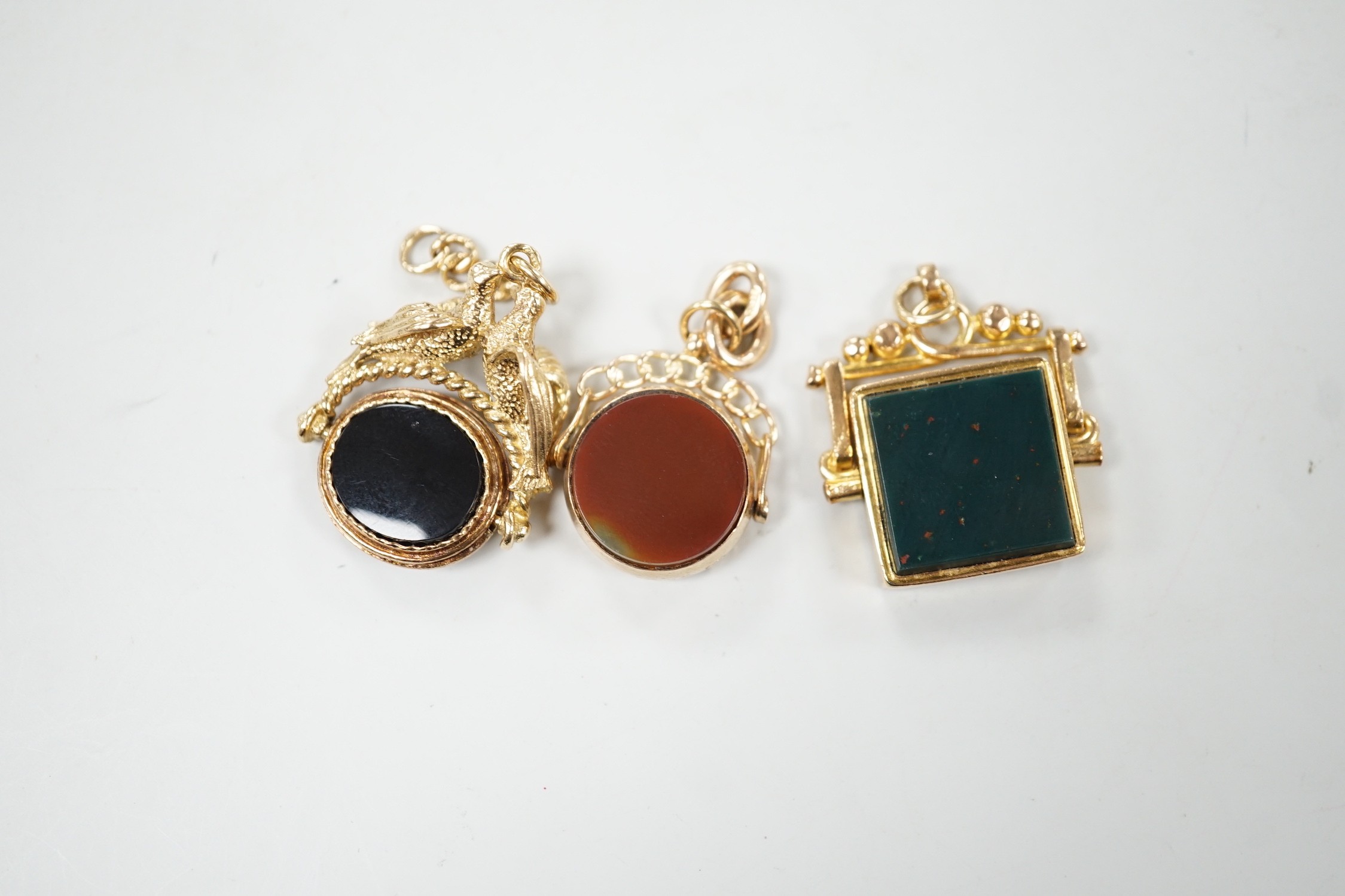 Two early 20th century 9ct gold and chalcedony set spinning fobs and one other yellow metal and chalcedony set spinning fob with twin bird finial, largest 31mm.